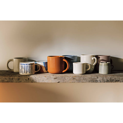 Collection of ceramic mugs on a wooden shelf with a neutral background
