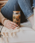 Person sitting on a couch with a glass of iced coffee and a blanket