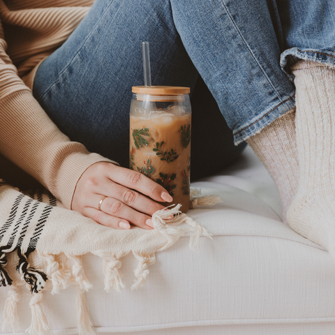 Person sitting on a couch with a glass of iced coffee and a blanket