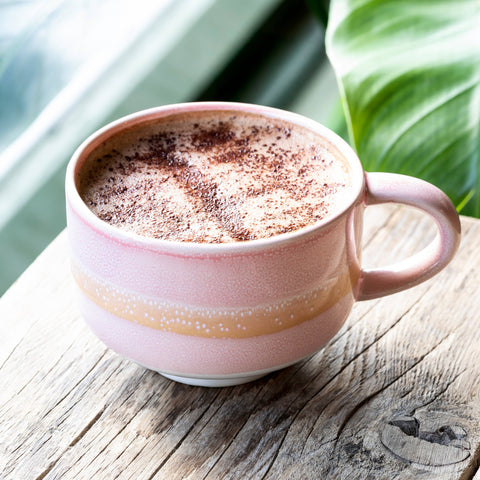 Pink mug with a hot beverage on a wooden surface with green leaves in the background