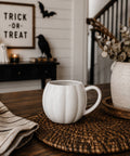 White ceramic mug on a woven mat with Halloween decorations in the background