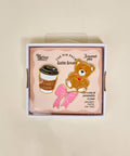 Box of enamel pins featuring a teddy bear, coffee cup, and pink bow design.