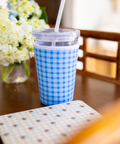 Blue checkered cup sleeve with a straw on a table with flowers in the background