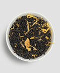 Black tea leaves with gold strands in a white bowl on a light gray background