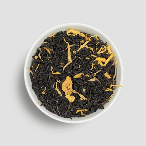 Black tea leaves with gold strands in a white bowl on a light gray background