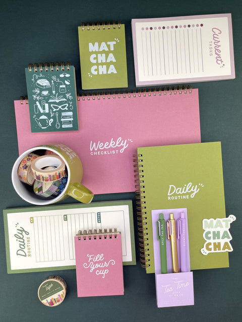 A coordinated stationery set arranged on a dark teal background, including multiple notebooks, a weekly checklist pad, a daily routine notebook, a habit tracker pad, washi tape, a mug, and pens in pastel colors. The set uses several colors in roughly similar prominence: pink, olive green, lavender, white, and dark teal, so the best constrained palette choice is Multicolor.