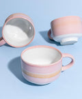 Three ceramic mugs with pink and white glaze on a light blue background