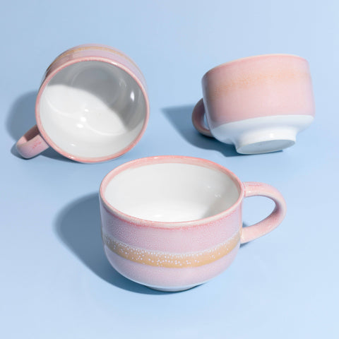 Three ceramic mugs with pink and white glaze on a light blue background