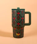 A dark green insulated travel mug with a festive red and green floral pattern, featuring a matching dark green handle and lid, set against a solid peach background.