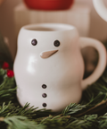White mug with a snowman face on a bed of greenery
