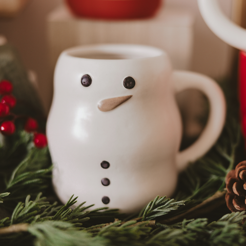 White mug with a snowman face on a bed of greenery