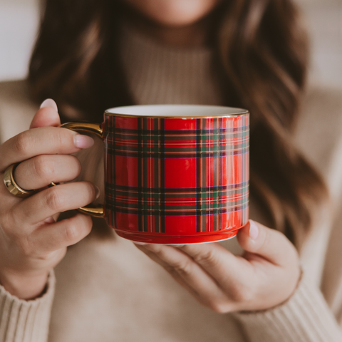 Red plaid mug held by a person wearing a beige sweater.