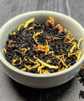 Tea leaves with floral elements in a white bowl on a dark surface - Little Prayer Tea Company 