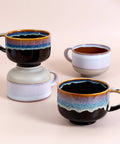 Four ceramic mugs with gradient coloring on a beige background