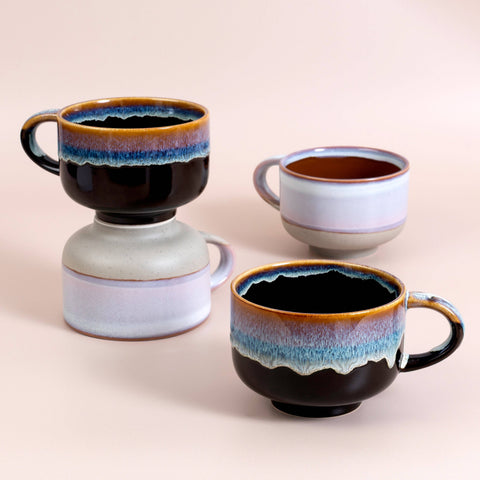 Four ceramic mugs with gradient coloring on a beige background