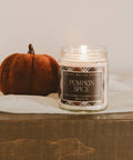 Pumpkin spice candle with a small pumpkin on a wooden surface