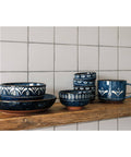 Set of blue ceramic dishes with white patterns on a wooden shelf against a tiled wall.