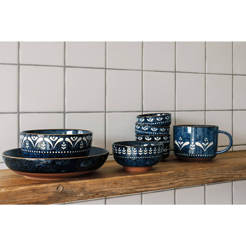 Set of blue ceramic dishes with white patterns on a wooden shelf against a tiled wall.