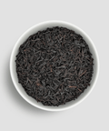 Black tea leaves in a white bowl on a light gray background - Little Prayer Tea Company 