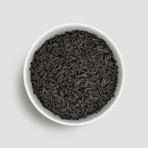 Black tea leaves in a white bowl on a light gray background - Little Prayer Tea Company 