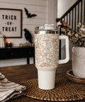 White tumbler with Halloween design on a wooden table, with decorative elements in the background.