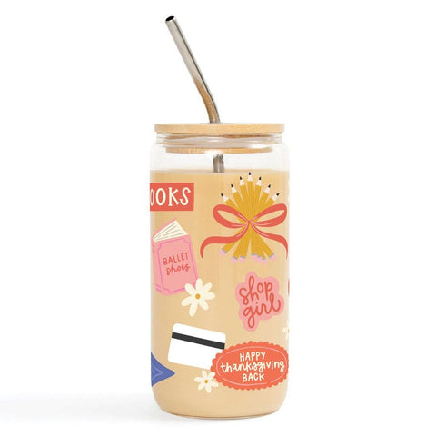 A clear glass can-shaped tumbler with a light wood lid and metal straw, decorated with colorful retro-style graphics including a yellow bow, pink text reading 'shop girl', white flowers, and a red 'HAPPY thanksgiving BACK' badge on a white background.