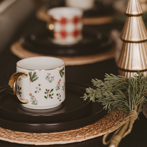Decorative mug with floral design , surrounded by greenery and a gold Christmas tree.