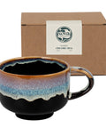 Nova Ceramics ceramic mug with multicolored glaze in front of a brown box.