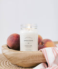 Candle labeled 'Georgia Peach' in a wooden bowl with peaches on a light background