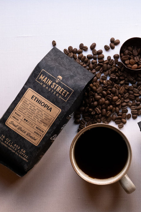 Coffee beans, a cup of coffee, and a package of Main Street Roasters Ethiopia coffee on a light surface.
