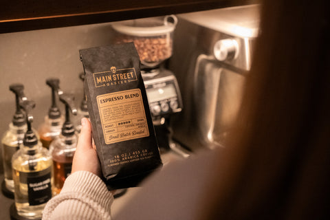 Person holding a package of Main Street Roasters Espresso Blend in a coffee shop setting.