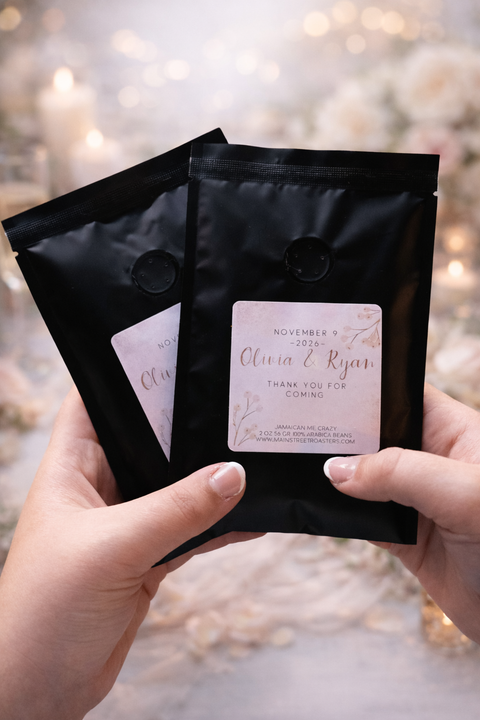 Two black coffee bags with personalized labels held by hands against a blurred background.
