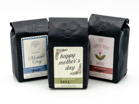 Three black coffee bags with Mother's Day-themed labels on a white background