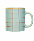 A ceramic mug with a light blue speckled glaze, decorated with a grid pattern of orange lines, and featuring a rustic gold rim, shown against a plain white background.
