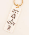 Keychain with 'Let's go for a coffee' text and coffee cup icon on a beige background