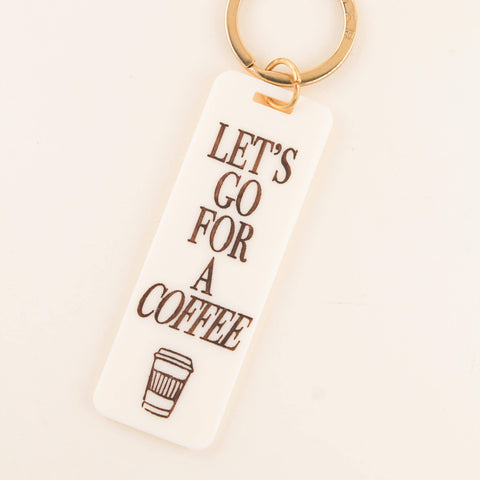 Keychain with 'Let's go for a coffee' text and coffee cup icon on a beige background