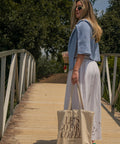 Woman walking on a wooden bridge holding a tote bag with 'Let's Go for Coffee' text.