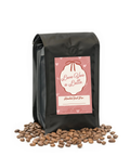 Black coffee bag with 'Love You a Latte' label and scattered coffee beans on a white background
