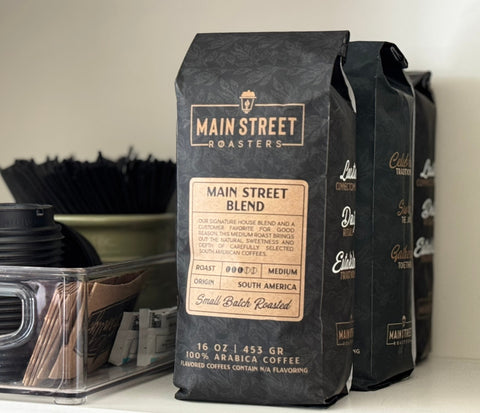 Black coffee bags with 'Main Street Roasters' branding on a shelf.