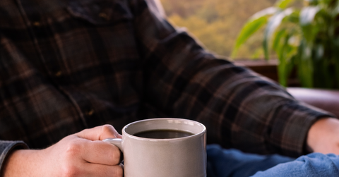 Person holding a mug of coffee by a window with a scenic view