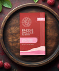 Little Prayer Tea Company Razzle Dazzle tea package on a wooden plate with raspberries and leaves.