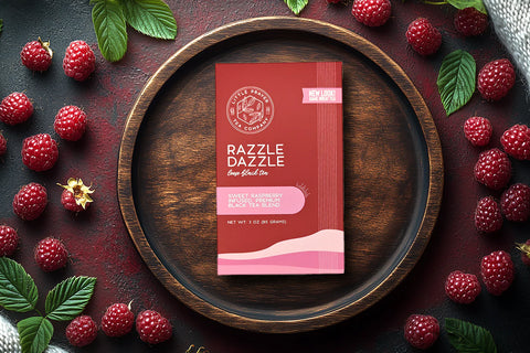 Little Prayer Tea Company Razzle Dazzle tea package on a wooden plate with raspberries and leaves.