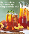 Peach iced tea with a pitcher and glasses on a wooden tray, surrounded by peaches.