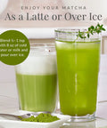 Two glasses of green matcha drink with a spoonful of matcha powder on a white surface.