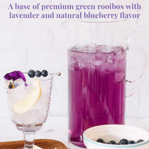 Purple drink in a pitcher with a glass of lemon and blueberries on a white background