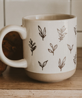 White mug with brown leaf patterns on a wooden surface