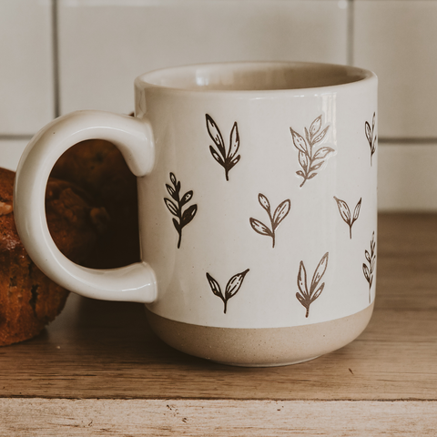 White mug with brown leaf patterns on a wooden surface