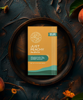 Little Prayer Tea Company tea package labeled 'Just Peachy' surrounded by peaches and leaves on a dark surface