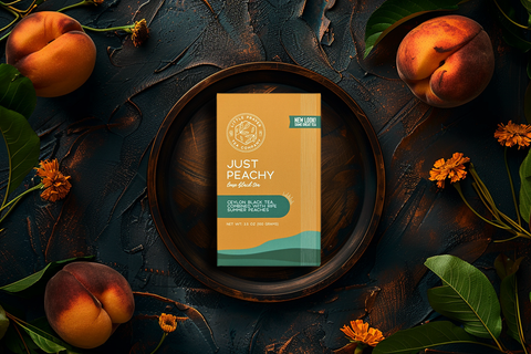 Little Prayer Tea Company tea package labeled 'Just Peachy' surrounded by peaches and leaves on a dark surface
