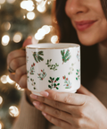 Person holding a mug with Christmas-themed design in front of a blurred festive background
